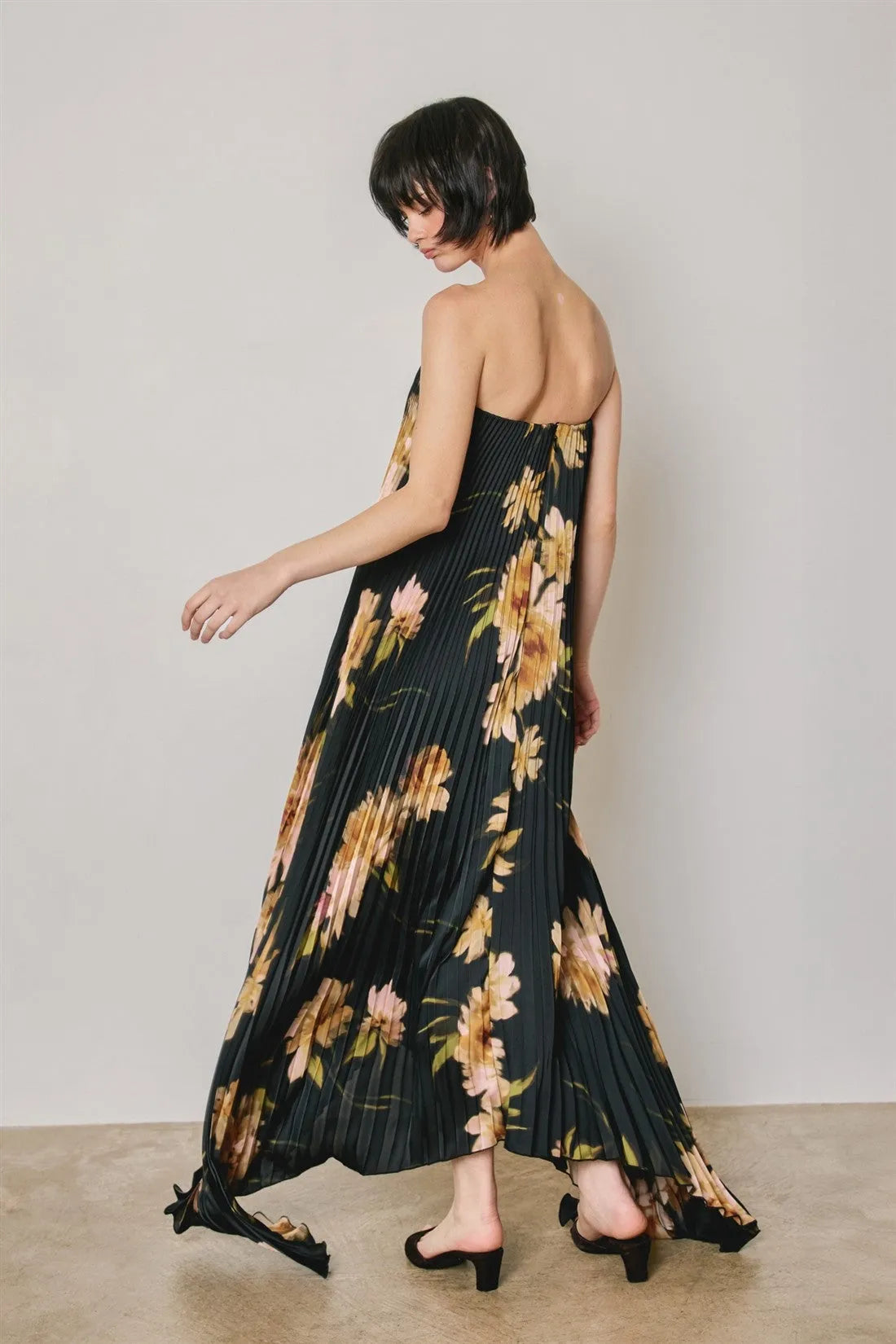 Black floral strapless pleated maxi column dress with gold and pink floral pattern and off-the-shoulder design