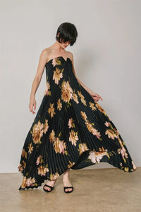 A black floral strapless pleated maxi column dress featuring vibrant peach and gold floral patterns in soft pink tones