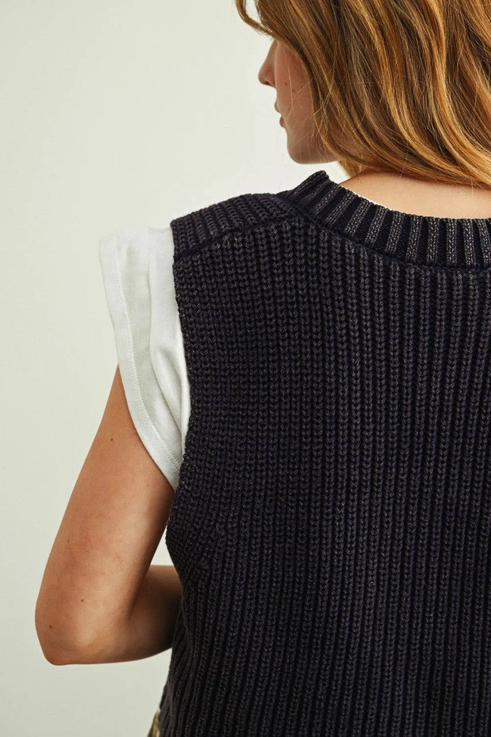 Black ribbed knit v-neck sweater vest worn over a white jersey top in sweater vest with jersey top combo set