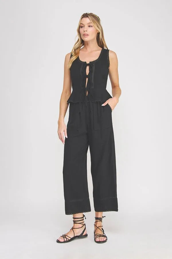 Black sleeveless linen blend jumpsuit with peplum waist, ties lace front detail, and scalloped hem in women’s boho chic clothing