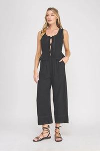 Black sleeveless linen blend jumpsuit with peplum waist, ties lace front detail, and scalloped hem in women’s boho chic clothing
