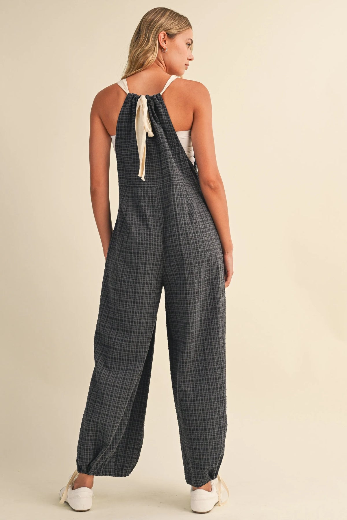 Black and white drawcord waistline plaid wide-leg jumpsuit with adjustable shoulder straps tied in a bow and adjustable ankles