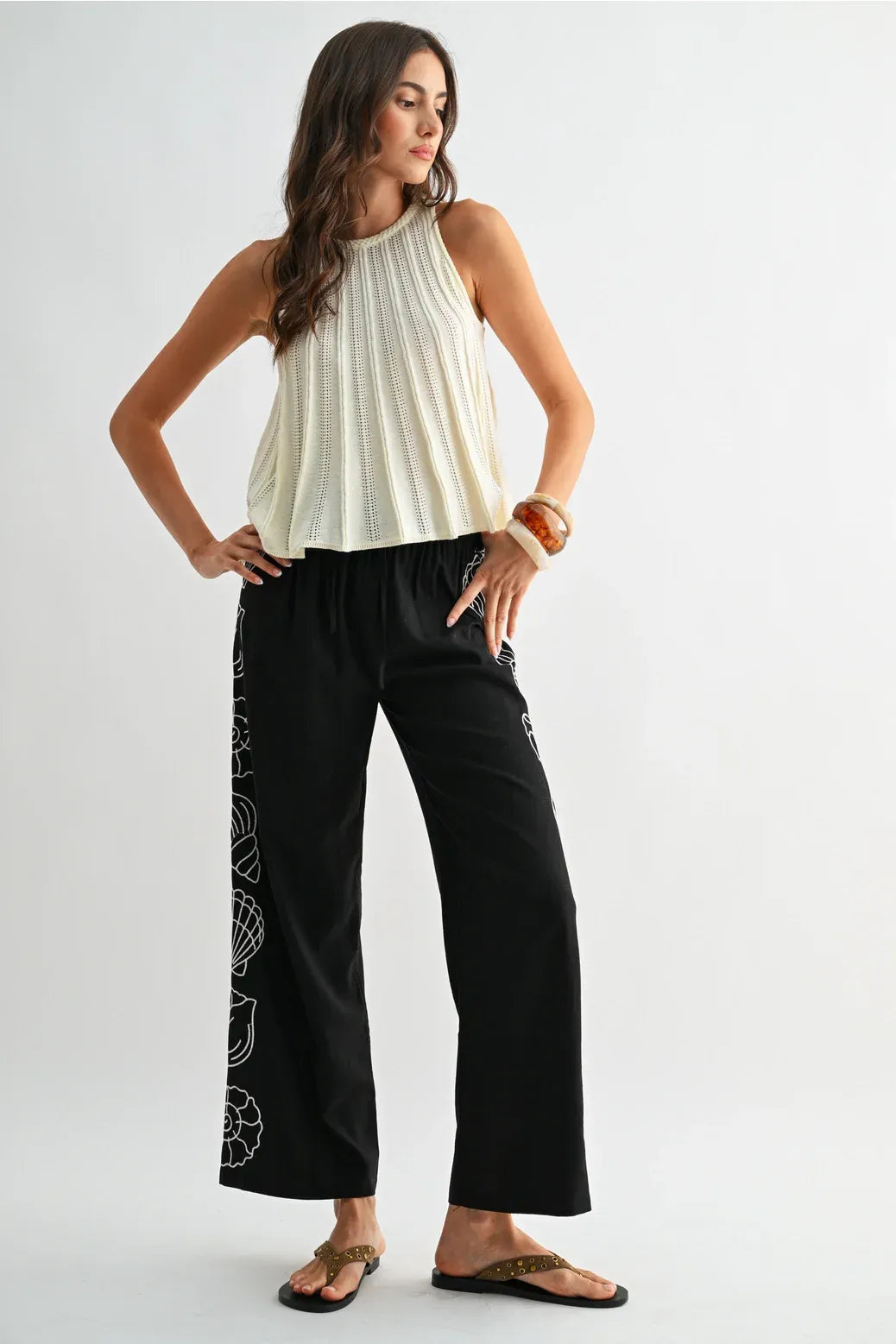 Black wide-leg pants with white shell embroidery along the side seam paired with a flared hem sleeveless knit top