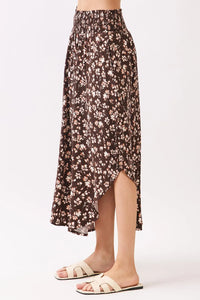 A flowing brown floral midi skirt with a high-waisted floral smocked waistband and asymmetrical hemline