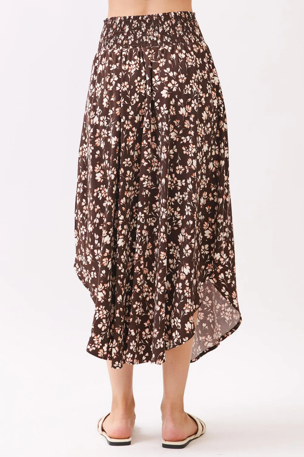 A flowing brown floral midi skirt with a high-waisted smocked waistband and asymmetrical hemline