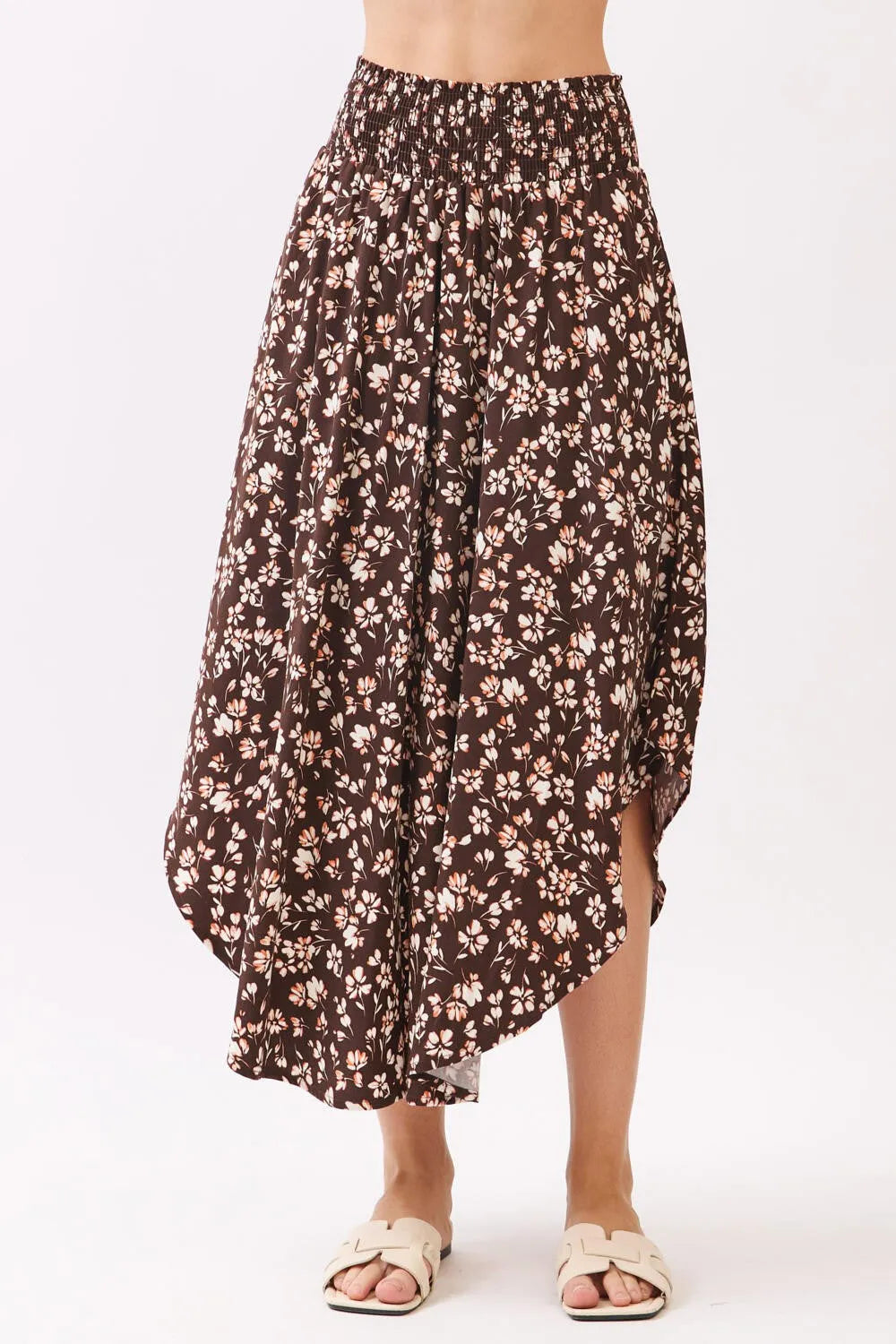 A flowing brown floral midi skirt with a high-waisted elasticated smocked waistband and asymmetrical hemline