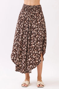 A flowing brown floral midi skirt with a high-waisted elasticated smocked waistband and asymmetrical hemline