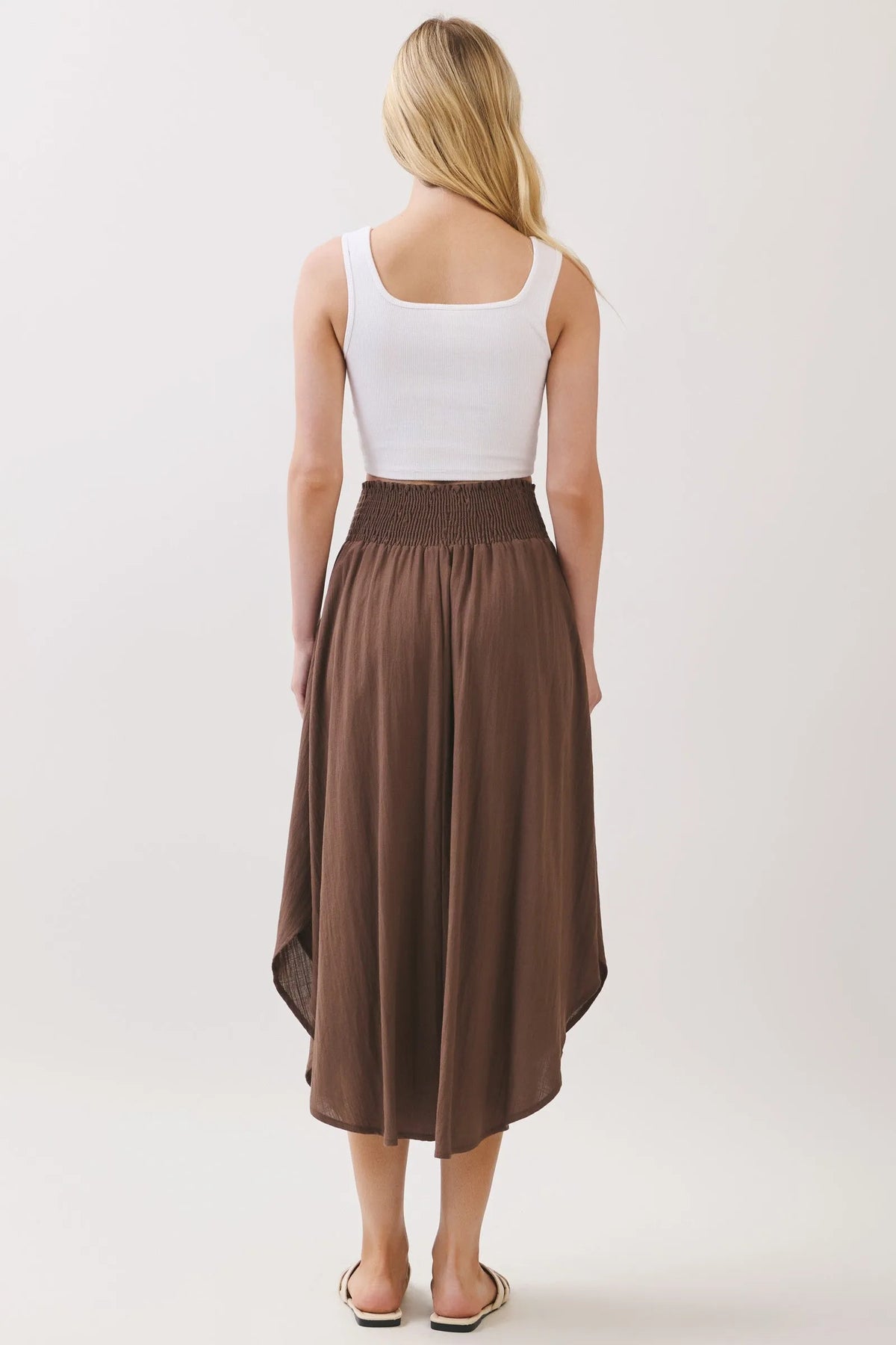 A flowing brown lined midi skirt with smocked waistband and rounded hem midi featuring an asymmetrical hemline