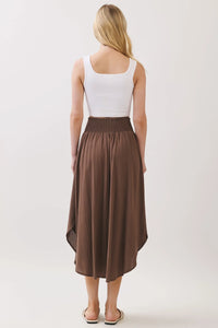A flowing brown lined midi skirt with smocked waistband and rounded hem midi featuring an asymmetrical hemline