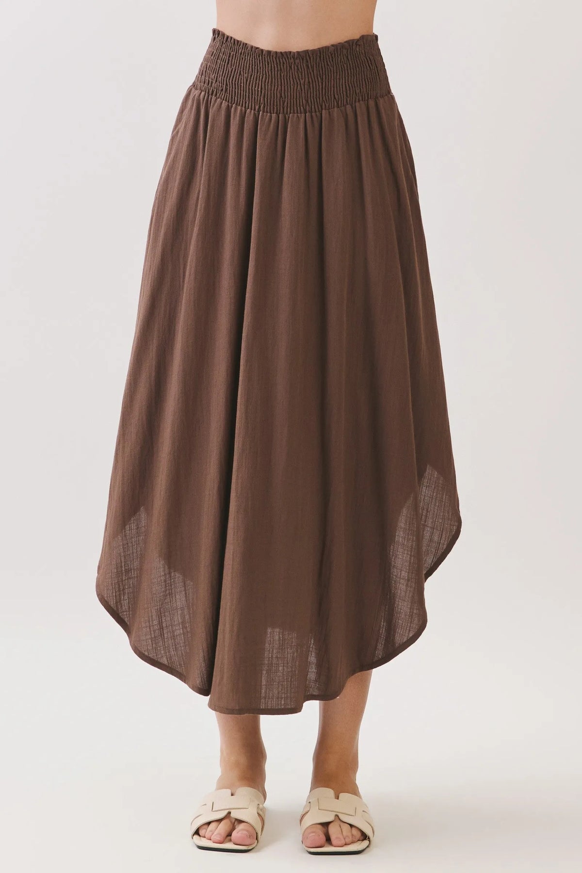 A flowing brown rounded hem midi skirt with smocked waistband lined and sheer textured panels at the hem