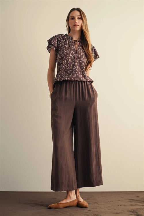 Brown wide leg pants with elastic waist, side pockets, soft flowing fabric, and subtle vertical pleats