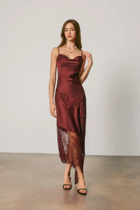 A flowing burgundy satin midi slip dress with asymmetrical lace trim along the hem and side slit