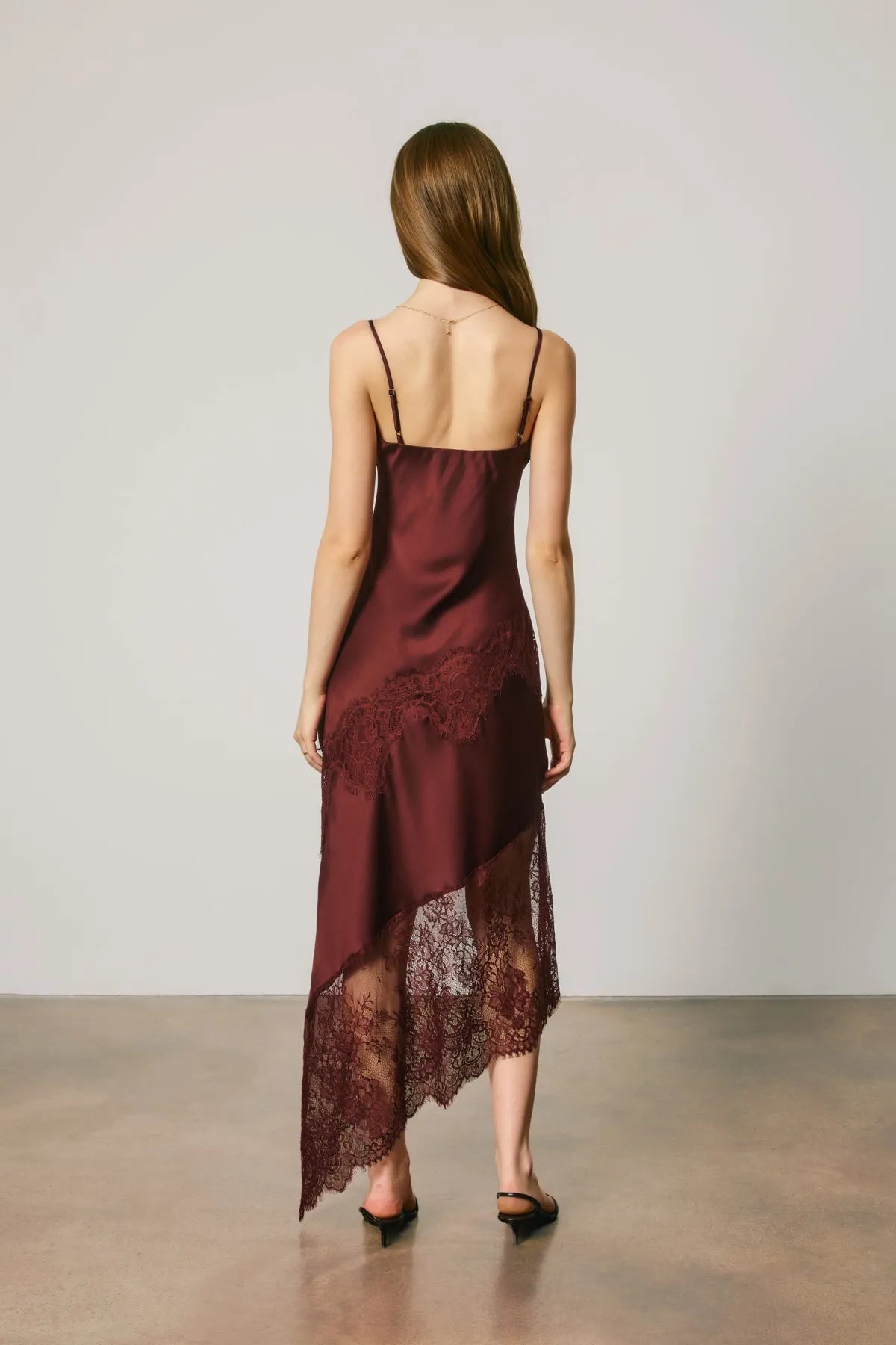 A burgundy satin slip dress featuring delicate asymmetrical lace trim along the hemline