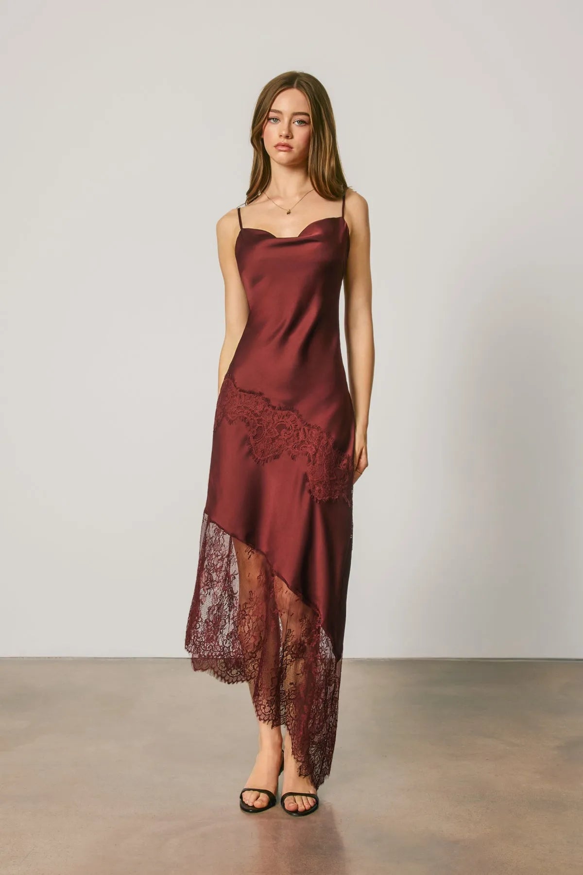 A flowing burgundy satin slip dress with asymmetrical lace trim and intricate lace detailing along the hemline