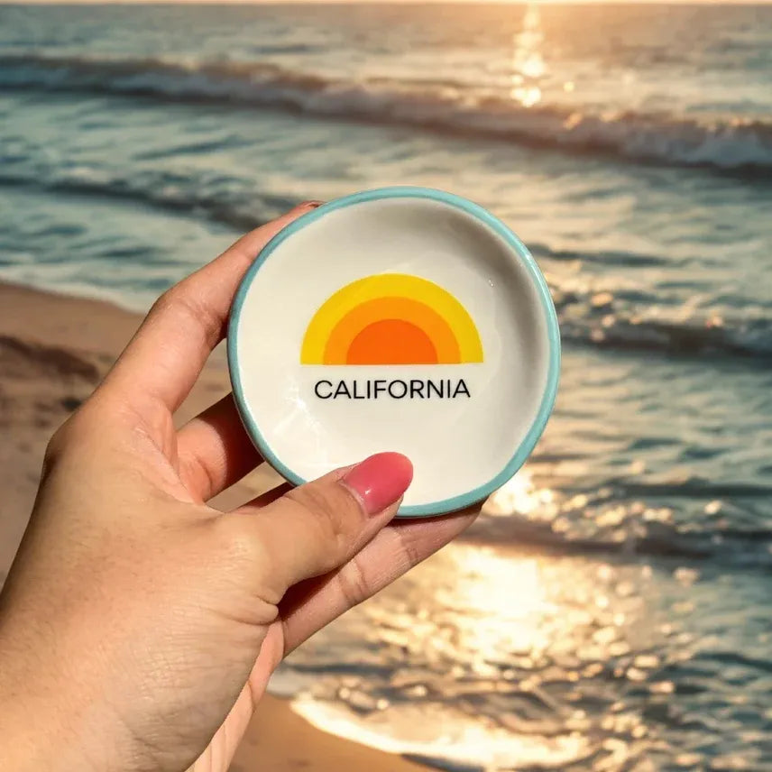 A ceramic ring dish california with a light blue rim white interior and yellow orange sun rainbow design