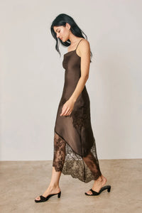 A flowing chocolate-brown satin slip dress featuring asymmetrical lace trim with intricate black lace detailing