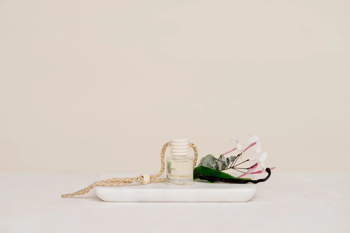 Hanging car fragrance diffuser in clear glass bottle with white cap and braided rope handle filled with pale liquid car diffuser