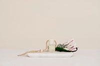 Hanging car fragrance diffuser in clear glass bottle with white cap and braided rope handle filled with pale liquid car diffuser