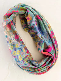 A colorful floral infinity scarf in soft pastel tones with blue garden patchwork on a light blue background