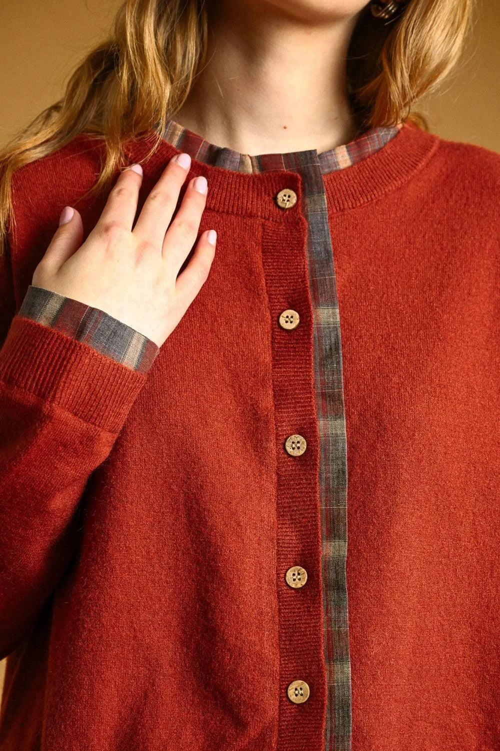 A cozy rust-colored knit cardigan with plaid contrasted button trim and wooden buttons down the front