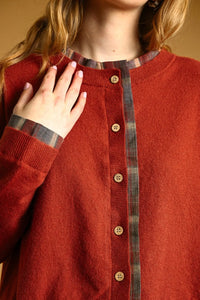 A cozy rust-colored knit cardigan with plaid contrasted button trim and wooden buttons down the front