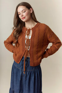 A cozy rust-colored knitted hole stripe bows front tie cardigan with intricate cable patterns and bow closure
