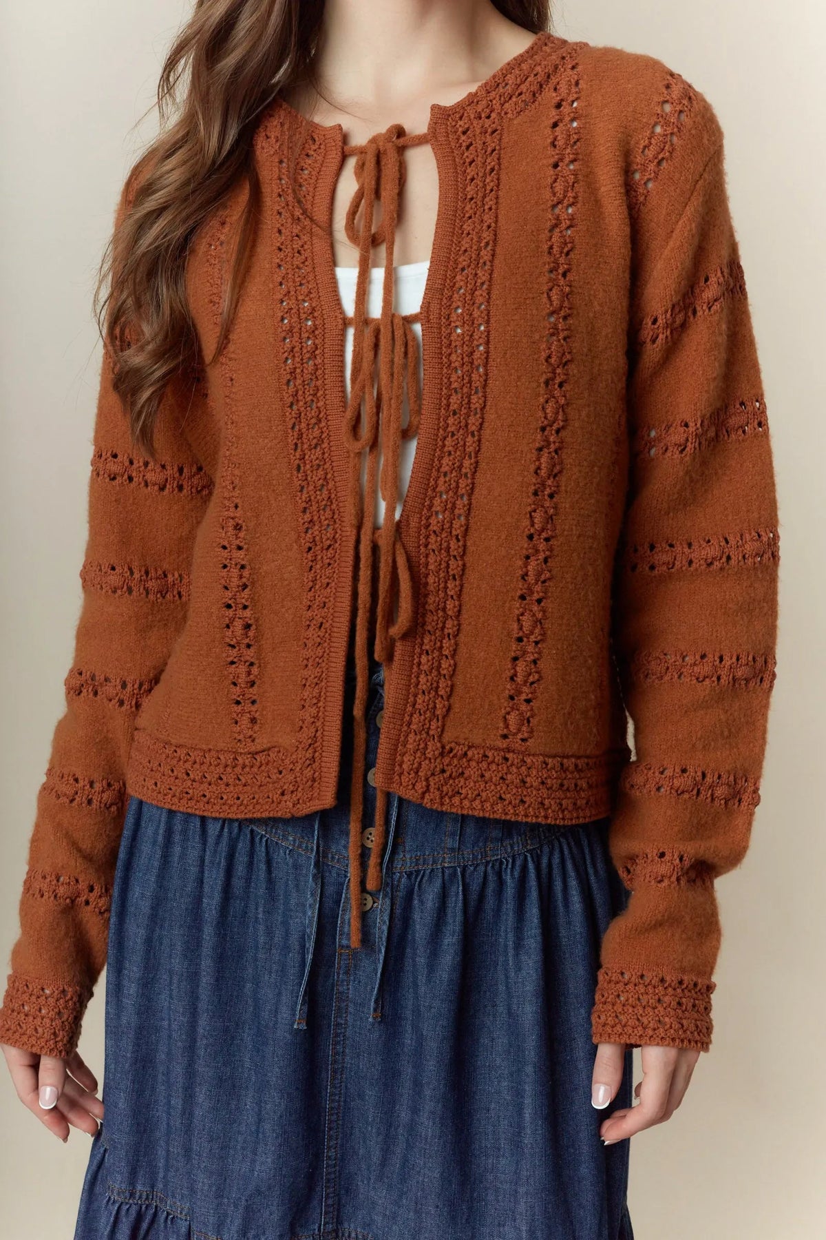 A cozy rust-orange knitted cardigan with hole stripe bows lace detailing and a front tie closure