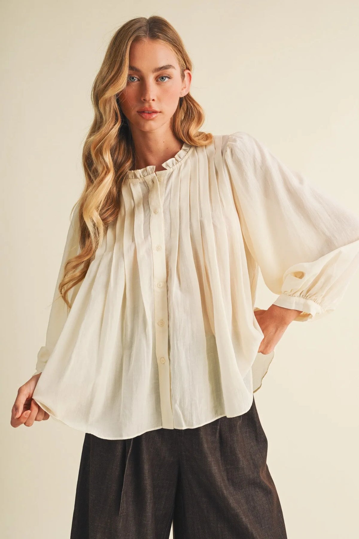 Cream-colored loose-fitting blouse with puffed sleeves featuring a pintuck bib ruffle collar detail