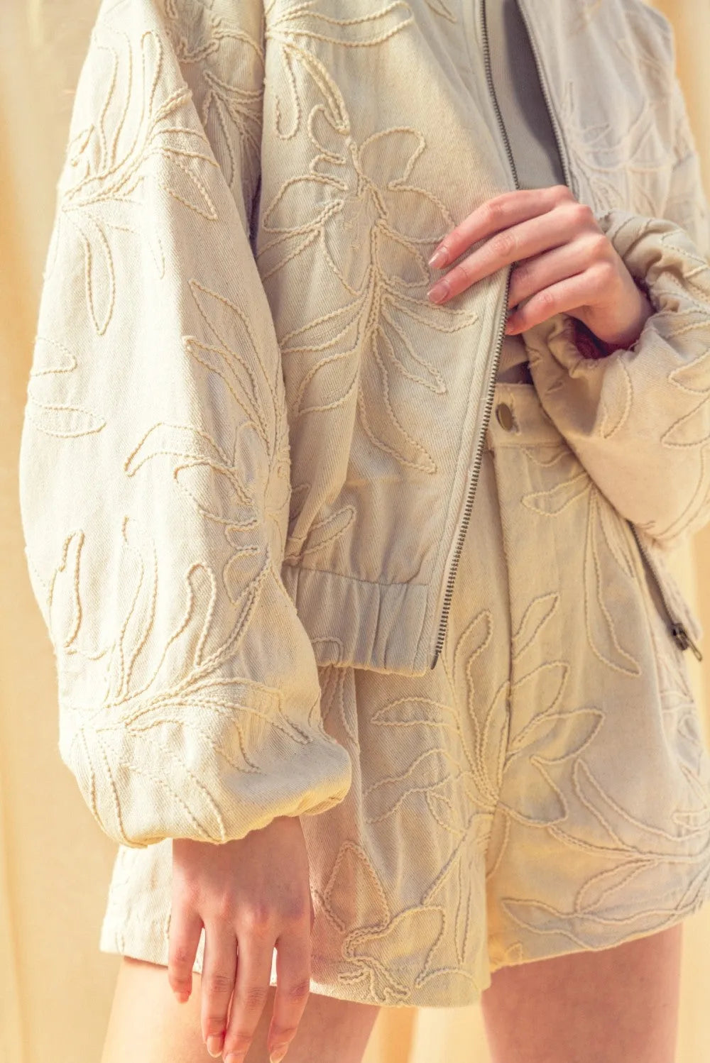 Cream-colored floral jacquard zip up jacket with intricate matching floral embroidery, zippered front, and elastic cuffs