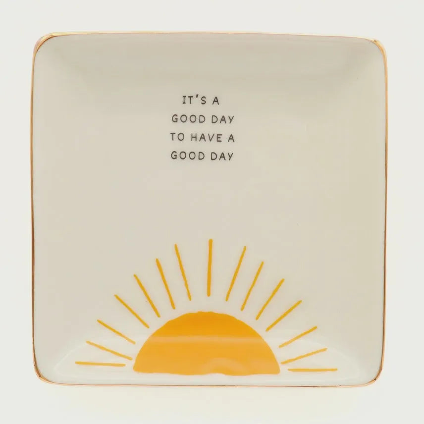 Cream-colored ceramic trinket tray with gold rim featuring a yellow sun and good day phrase in black lettering