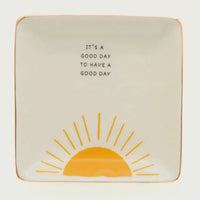 Cream-colored ceramic trinket tray with gold rim featuring a yellow sun and good day phrase in black lettering