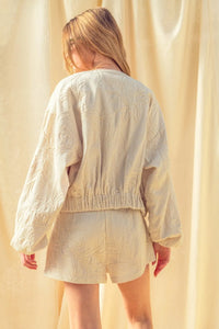 Cream-colored floral jacquard zip up jacket with embroidered floral patterns and elastic waistband for comfortable fit