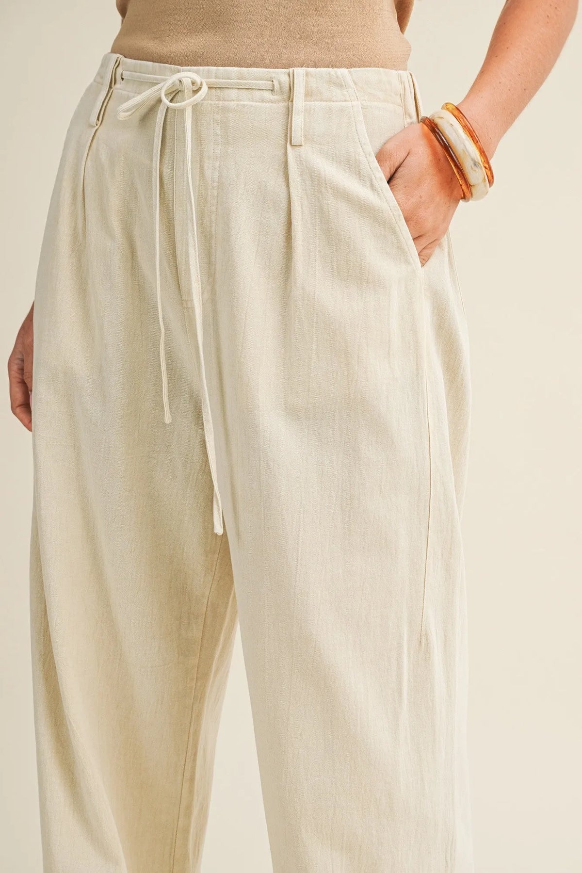 Cream-colored pleated waist wide leg dyed pants with a drawstring waistband and relaxed high-waisted fit