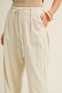 Cream-colored pleated waist wide leg dyed pants with a drawstring waistband and relaxed high-waisted fit