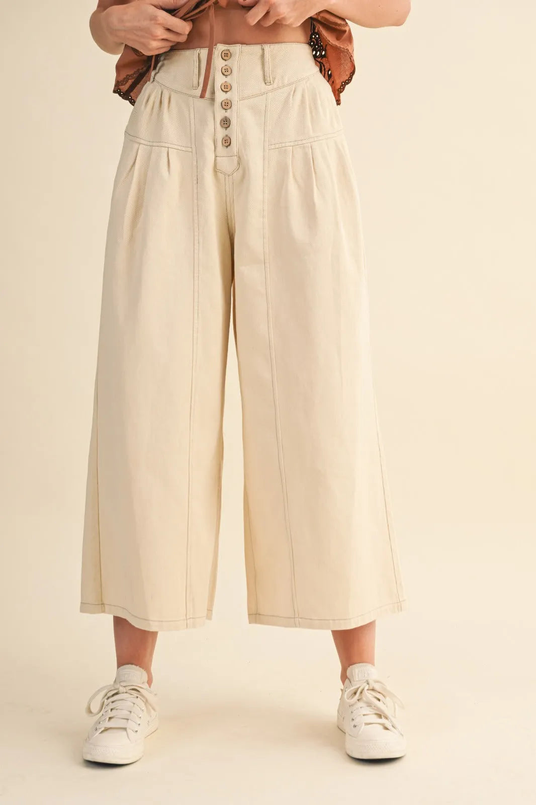 Cream-colored high rise super wide leg trousers with button-front closure and pleated detailing in crop denim style