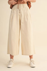 Cream-colored high rise super wide leg trousers with button-front closure and pleated detailing in crop denim style