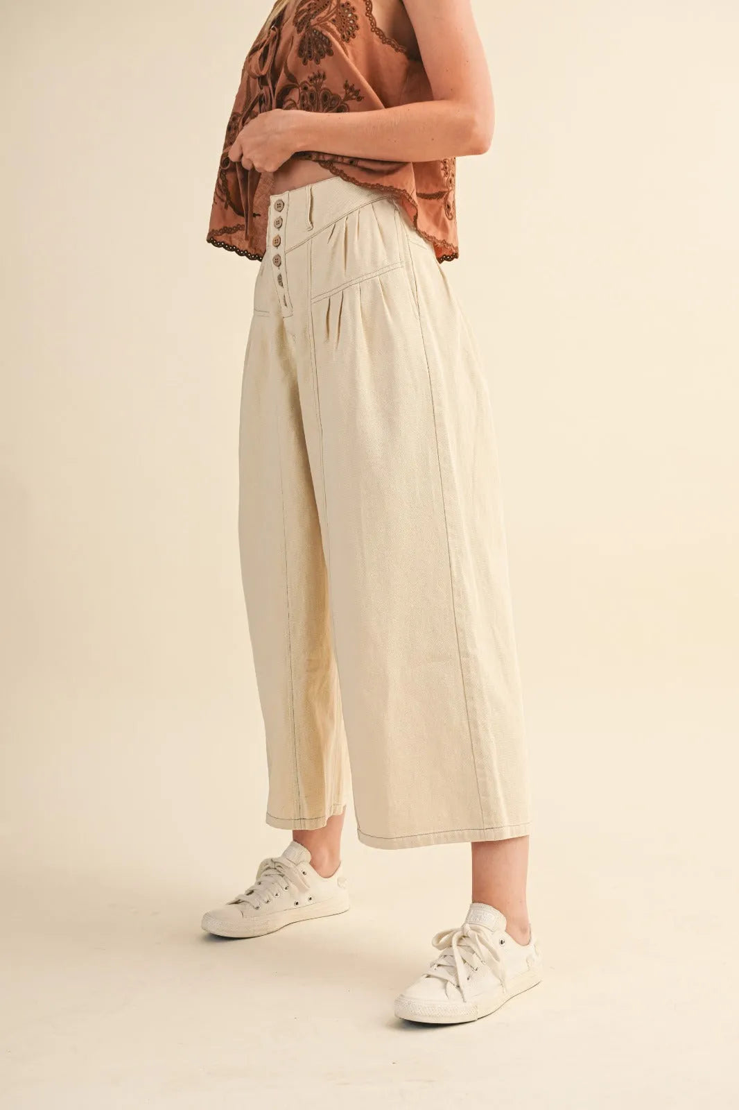 Cream-colored high rise super wide leg trousers with button-front closure and subtle pleats
