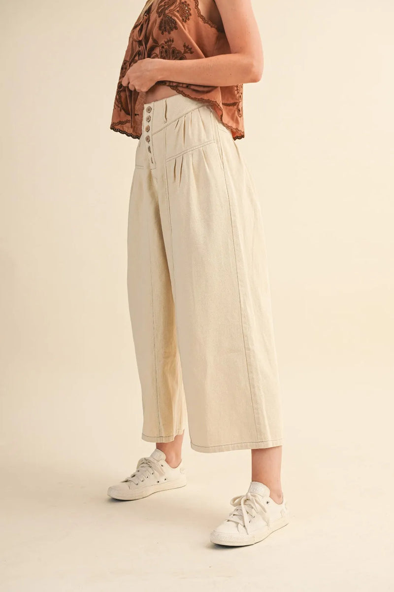 Cream-colored high rise super wide leg trousers with button-front closure and subtle pleats
