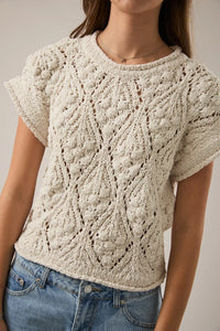 A cream-colored intricately knitted extended shoulder sweater top with short sleeves and a textured leaf pattern