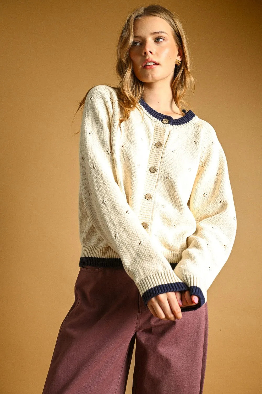 Cream-colored pointelle effect knit cardigan with navy blue trim and button closures for stylish layering