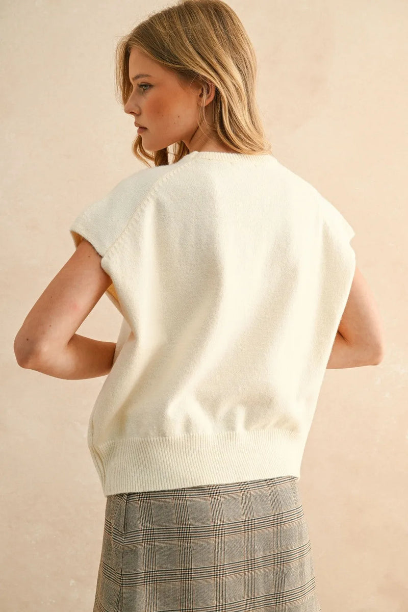 Loose fit cream-colored knit sleeveless top with ribbed hem and relaxed fit, ideal layered with olive green short sleeve sweater