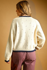 Cream-colored pointelle effect knit cardigan with navy blue ribbed trim and embroidered stars on the back