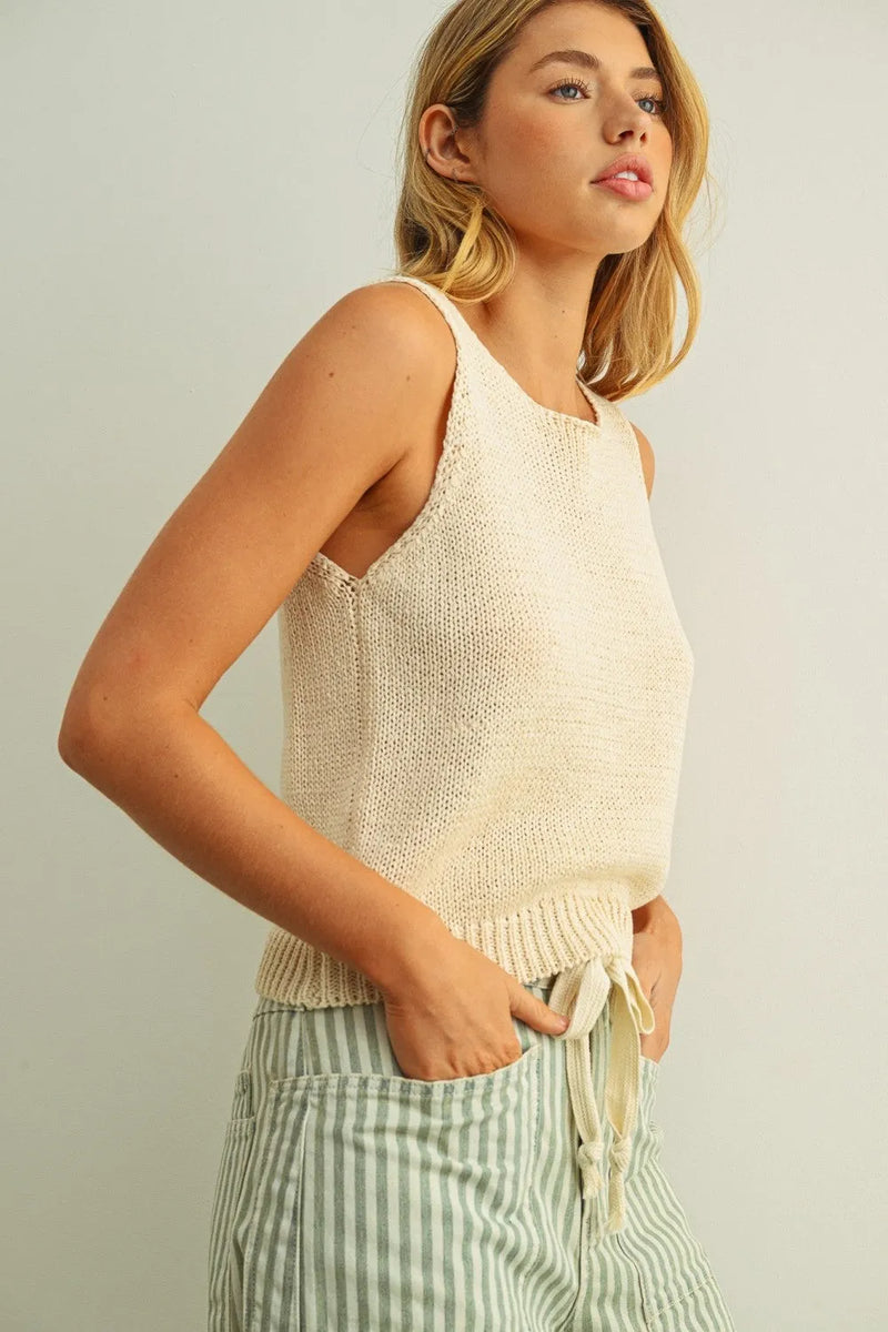 Cream-colored sleeveless roundneck knitted top with ribbed hem and drawstring tie at the waist