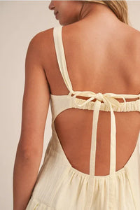 Back view of a cream-colored shirring bra cotton mini dress with thin straps tied into a bow and open-back design