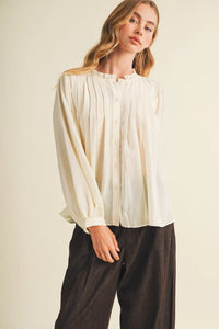 Cream-colored long-sleeved blouse with pintuck bib ruffle and ruffle collar featuring vertical pleats down the front