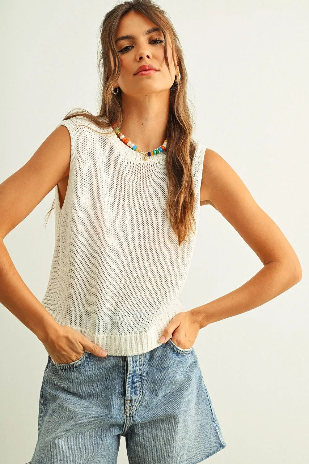 Cream-colored sleeveless round neck knitted top with open-knit design and ribbed hem for stylish layering