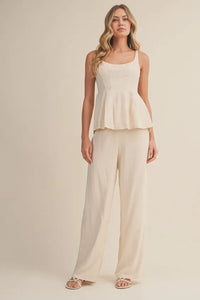 Cream-colored high rise wide leg pants paired with a matching peplum top featuring square neckline and thin straps