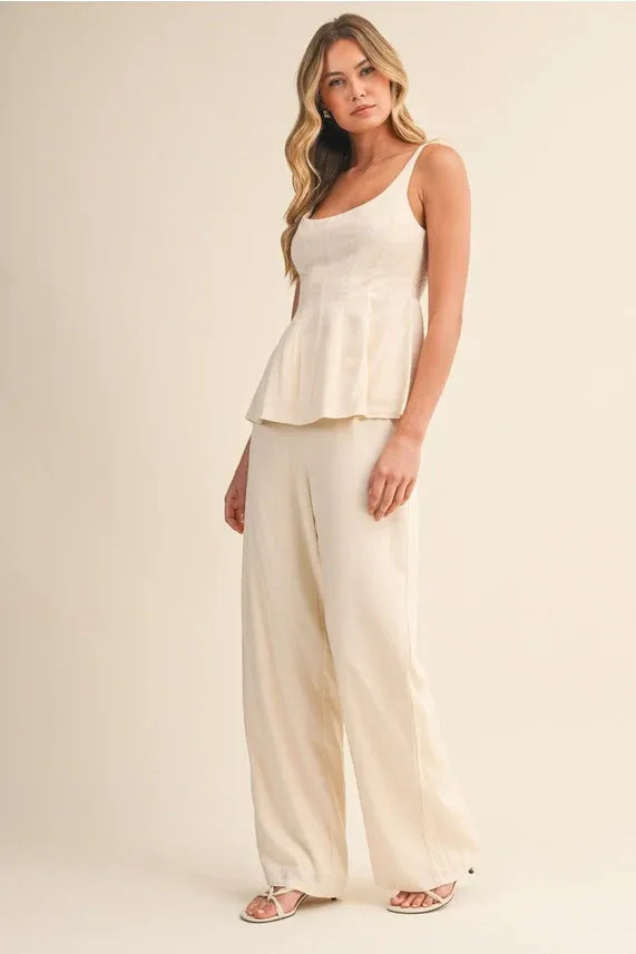 Cream-colored scoop neck zipper back blouse with thin straps and flowing ruched peplum hemline for elegant wear