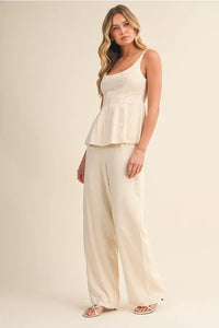 Cream-colored scoop neck zipper back blouse with thin straps and flowing ruched peplum hemline for elegant wear