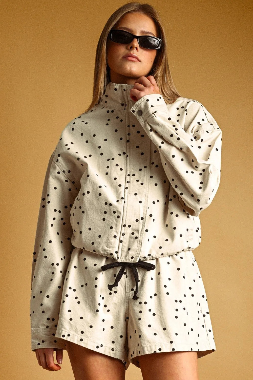Cream-colored polka dot high neck utility jacket with black dots and adjustable drawstring waist for versatile wear